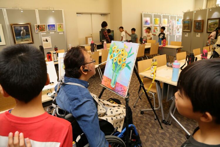 口を使って描く様子を見学する児童(阪急西宮ガーデンズにて)